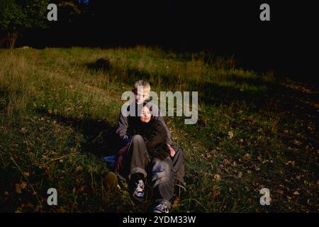 couple adolescent de 15 ans dans l'amour mensonge, assis sur l'herbe dans le parc entouré de feuilles d'automne tombées Banque D'Images