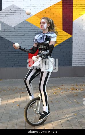 Fille clown monte un monocycle et jongle avec des balles à l'extérieur Banque D'Images