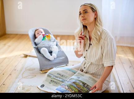 Mère regardant la propriété dans le papier avec bébé en arrière-plan Banque D'Images