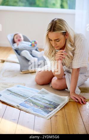 Mère regardant la propriété dans le papier avec bébé en arrière-plan Banque D'Images