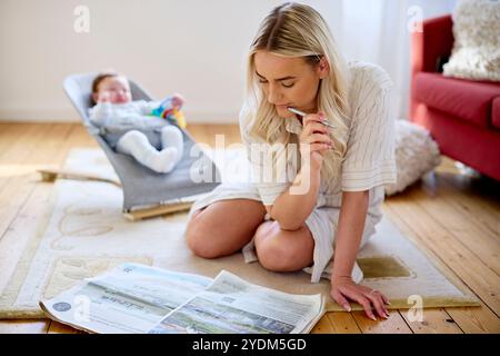 Mère regardant la propriété dans le papier avec bébé en arrière-plan Banque D'Images