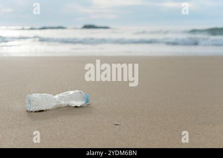 Une bouteille en plastique vide repose sur la plage de sable déserte Banque D'Images