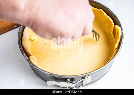 La pâte, disposée dans un plat allant au four, la main fait des piqûres dans la pâte avec une fourchette. Recette de tarte. Photo de haute qualité Banque D'Images