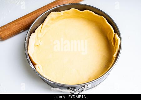 La pâte est disposée dans un plat allant au four, l'étape suivante est le remplissage. sur une table blanche avec un rouleau à pâtisserie en bois. Photo de haute qualité Banque D'Images