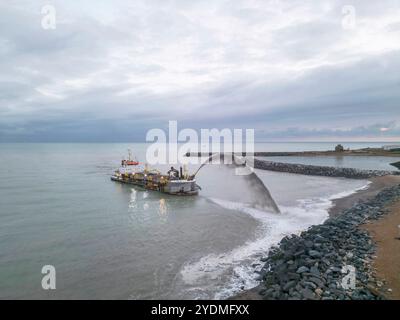 chaland de drague pulvérisant du gravier sur la plage du port souverain d'eastbourne pour remplacer le gravier perdu Banque D'Images