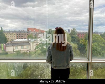 Copenhague, Danemark - 9 juillet 2022 : moment contemplatif : femme regardant le paysage urbain à travers une grande fenêtre à la Galerie nationale du Danemark Banque D'Images