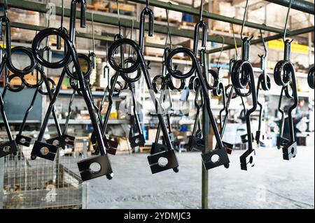 Gros plan de pièces métalliques revêtues de noir suspendues dans une usine ou un atelier, prêtes pour le traitement ou l'assemblage. Banque D'Images