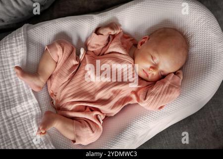 Adorable bébé fille nouveau-né dans des vêtements roses dormir paisiblement tout en nichant dans Cocoon blanc confortable, moment serein d'innocence et de confort dans Cozy Ind Banque D'Images