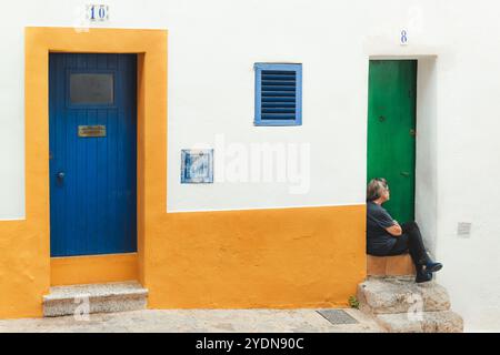 Ibiza, Espagne - 8 octobre 2023 : scène de rue animée dans la ville d'Ibiza, avec des portes colorées et un moment serein de la vie locale contre un médite rustique Banque D'Images