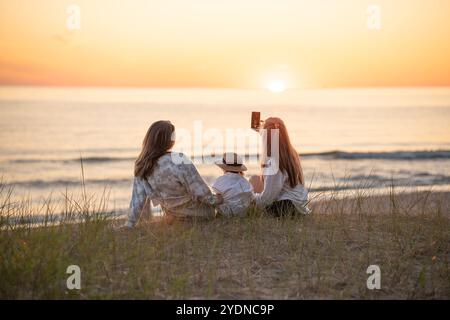 Vue arrière de deux amies caucasiennes et un enfant faisant selfie au coucher du soleil sur le bord de mer Baltique Banque D'Images