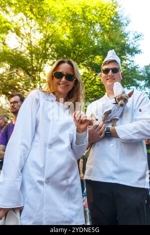 Un homme et une femme en vestes de chef souriant à l'extérieur, tenant un petit chien habillé dans une tenue de chef assortie nyc chien défilé octobre 2024 Banque D'Images