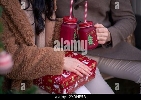 Un couple partage un moment de joie pendant la saison des fêtes, tenant des boissons festives tout en étant assis à côté d'un sapin de Noël joliment décoré et d'une WR Banque D'Images