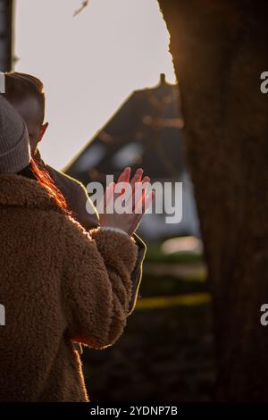 Alors que le soleil se couche, un couple se tient près les uns des autres, leurs mains éclairées d'une lueur chaude. L'atmosphère chaleureuse reflète une connexion extérieure paisible Banque D'Images