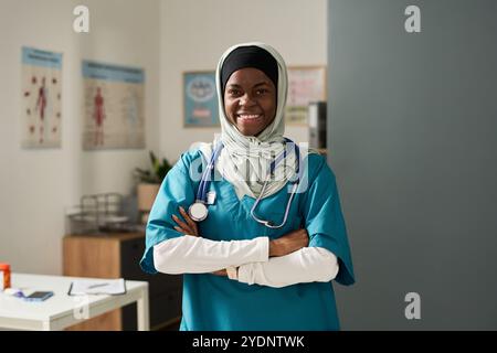 Infirmière musulmane souriant chaleureusement dans le cabinet médical avec stéthoscope autour du cou, mettant en valeur une tenue professionnelle et un comportement compatissant Banque D'Images