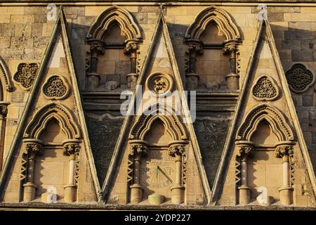 Gros plan d'un mur de pierre avec des sculptures complexes. Fenêtres triangulaires, cintrées avec des colonnes ornées et un cadran solaire au centre à York, North Yorkshire, Banque D'Images