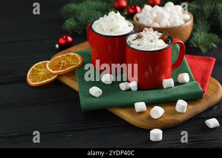 Savoureuses boissons chaudes au cacao avec de la crème fouettée dans des tasses et des guimauves sur une table en bois noir, gros plan Banque D'Images