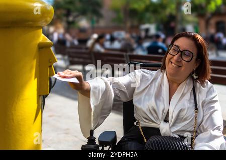 Femme en fauteuil roulant envoyant une lettre à Urban Mailbox Banque D'Images