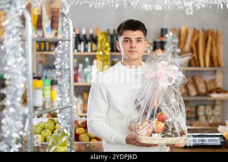 Guy achetant des aliments de Noël présents dans la boutique - tenant un cadeau magnifiquement emballé avec de la nourriture et de l'alcool Banque D'Images