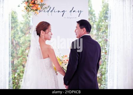 Petit mariage - le prêtre est présent, la mariée et le marié tiennent leurs bouquets de mariage, se tiennent la main et partagent un beau moment avec la famille et les amis Banque D'Images