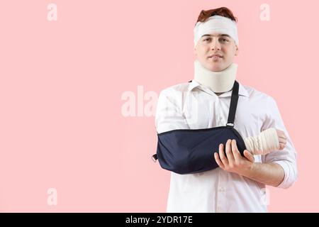 Jeune homme blessé après un accident avec bras cassé sur fond rose Banque D'Images