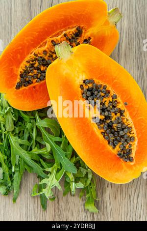 Fruit de papaye et rucola sur un fond en bois clair. Tranches de papaye douce sur fond de bois, papayes coupées en deux, espace de copie pour le texte Banque D'Images