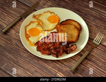 Une grande assiette de délicieux et nutritif petit déjeuner sur une table en bois, œufs brouillés, bacon frit et pain grillé, couverts à proximité. Gros plan. Banque D'Images