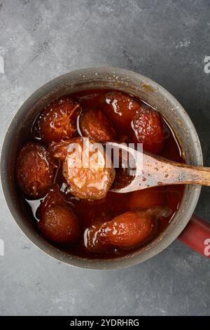 ambarella ou confiture de prunes de juin ou marmelade dans une poêle avec une cuillère en bois, dessert juteux tropical doux aromatisé sur le dessus de la table, pris d'en haut avec espace de copie Banque D'Images