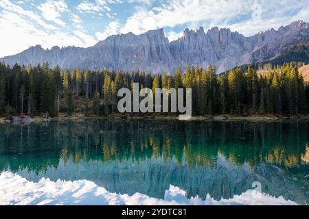 Au milieu des sommets imposants des Dolomites, un lac turquoise calme reflète la chaîne de montagnes escarpées et les forêts de pins luxuriantes sous un ciel lumineux, le lac Carezza ou Karersee Dolomites en Italie. Banque D'Images