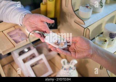 Vente de sachets aromatiques faits à la main : une femme à un marché remet un sachet artisanal à un client, mettant en valeur l'artisanat et les parfums naturels. Banque D'Images