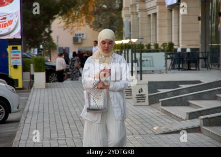 Boukhara, Ouzbékistan ; septembre,19,2024:une belle jeune femme musulmane vêtue d'un voile blanc coulant se tient contre la toile de fond enchanteresse de Boukhara Banque D'Images