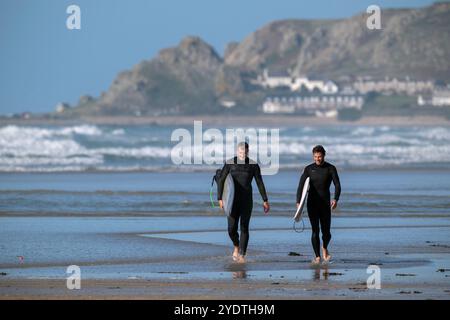 Deux surfeurs en combinaisons se promènent sur la plage en portant leurs planches après une séance de surf. Banque D'Images