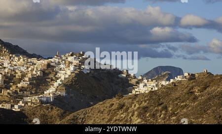 Un village s'étend sur une montagne sur un fond de nuages denses et un ciel bleu, village de montagne coloré, lumière du matin, Olymbos, Karpathos Banque D'Images