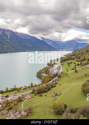 Paysage alpin avec un lac, des prairies verdoyantes et des bâtiments à flanc de colline sous les nuages, le lac de Brienz. Suisse Banque D'Images