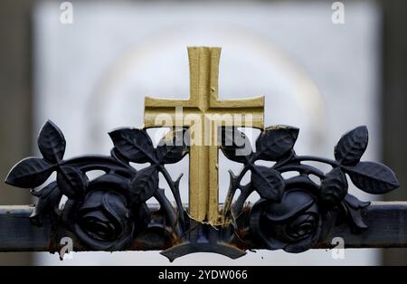 Croix dorée sur une clôture en fer forgé d'une tombe dans un cimetière Banque D'Images