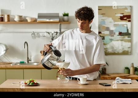 Dans une cuisine contemporaine, un beau jeune homme verse le café d'une bouilloire dans un verre, profitant de moments culinaires. Banque D'Images