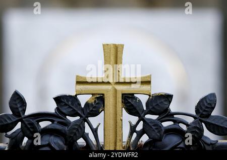 Croix dorée sur une clôture en fer forgé d'une tombe dans un cimetière Banque D'Images