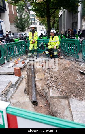 Travailleurs des services publics ouvriers travailleurs travaillant, barrières et tuyau de service noir creusant la chaussée dans la ville de Londres Angleterre Grande-Bretagne KATHY DEWITT Banque D'Images