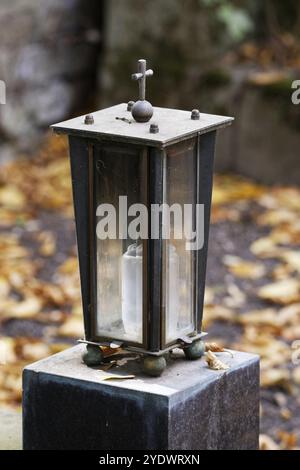 Lanterne funéraire en métal avec des fenêtres en verre sur une base en pierre devant un fond flou avec des feuilles d'automne Banque D'Images