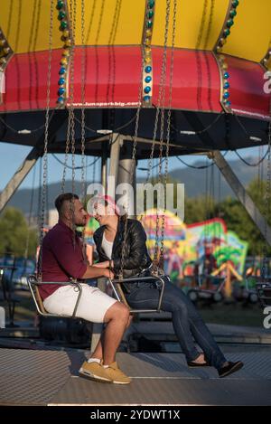 Jeune couple amoureux assis sur un carrousel à une fête foraine Banque D'Images