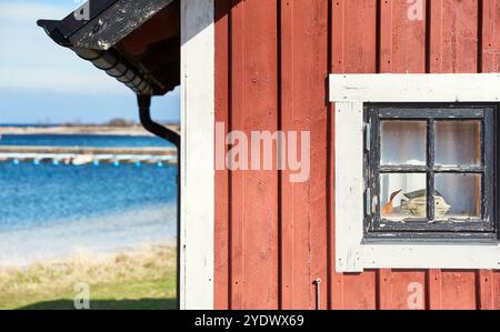 Détail estival suédois en bois rouge au bord de la mer avec une fenêtre carrée où un poisson est visible. Petite maison d'été en bord de mer dans un village de pêcheurs Banque D'Images