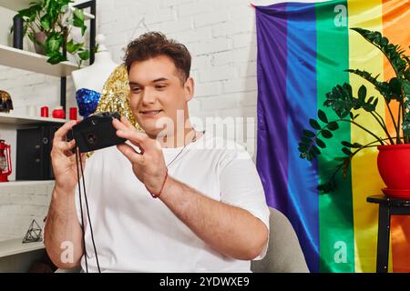 Une personne queer sourit tout en prenant un selfie dans un environnement coloré et sur le thème de la fierté. Banque D'Images