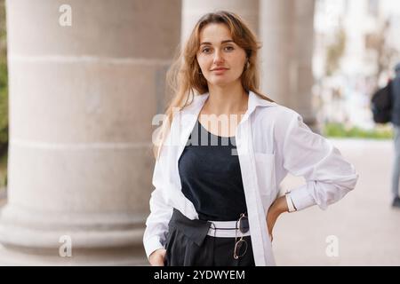 Jeune femme confiante en tenue urbaine chic posant contre Column. Banque D'Images