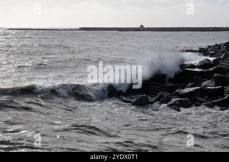 Lyme Regis, Dorset, Royaume-Uni. 25 octobre 2024. Une vue du Cobb avec une vague se brisant sur des marches et des rochers. Banque D'Images