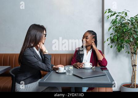 Deux jeunes femmes d'affaires heureuses et insouciantes assises à la cafétéria sur la pause café du travail et des problèmes de bureau. Profession professionnelle féminine d'affaires dis Banque D'Images