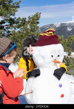 Deux enfants caucasiens faisant un bonhomme de neige dans les montagnes un jour d'hiver Banque D'Images