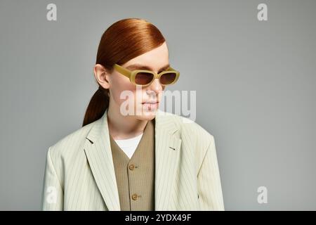 Un adolescent aux cheveux roux saisissants pose en toute confiance dans un ensemble chic et décontracté dans un studio élégant. Banque D'Images