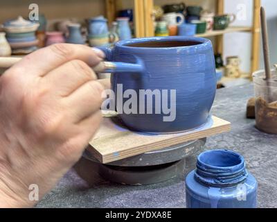 Le processus de peinture d'un vase en argile lors d'une masterclass de céramique. Savoir-faire et créativité en action. Le vase est recouvert de glaçure bleue, créati Banque D'Images