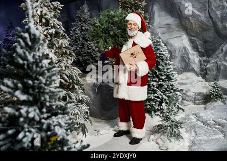 Une jolie figure du Père Noël se tient au milieu des arbres à feuilles persistantes, tenant un cadeau emballé. Banque D'Images