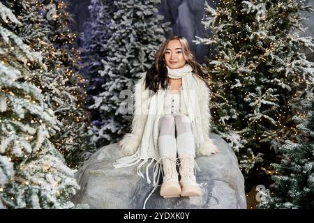 Un moment joyeux se déroule alors qu'une jeune personne est assise au milieu d'arbres enneigés décorés pour les vacances. Banque D'Images