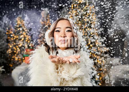 Une personne en tenue d'hiver souffle des flocons de neige dans l'air, entourée de décorations festives. Banque D'Images